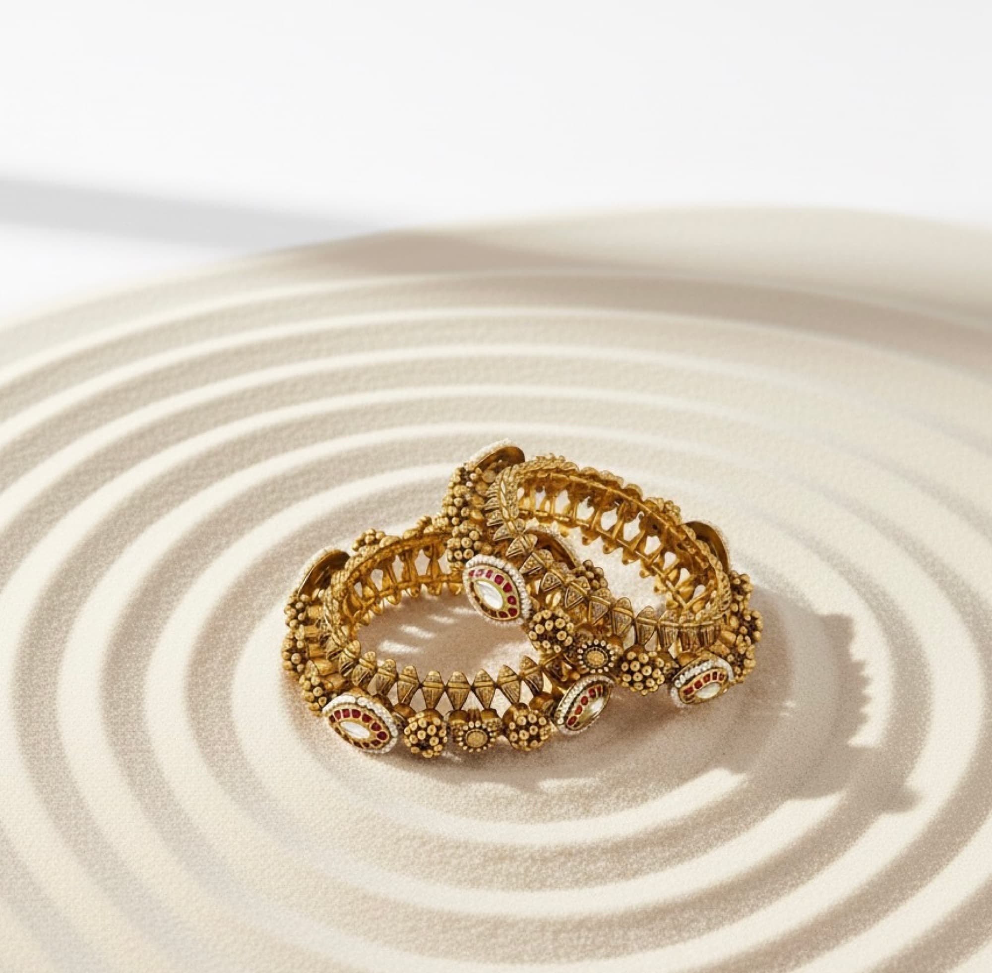 A pair of worked gold kada on rippled sand